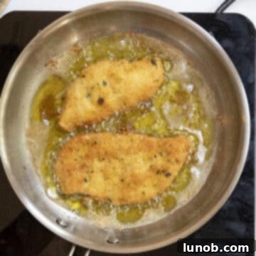 Chicken cutlets frying in oil and flipped over.