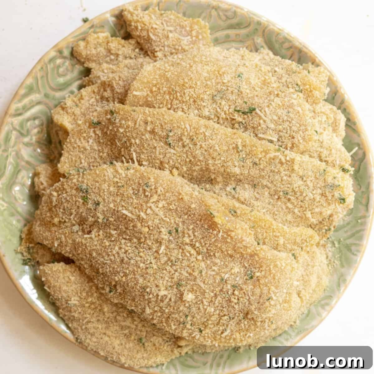 Breaded chicken breasts piled on a plate, ready to be fried.