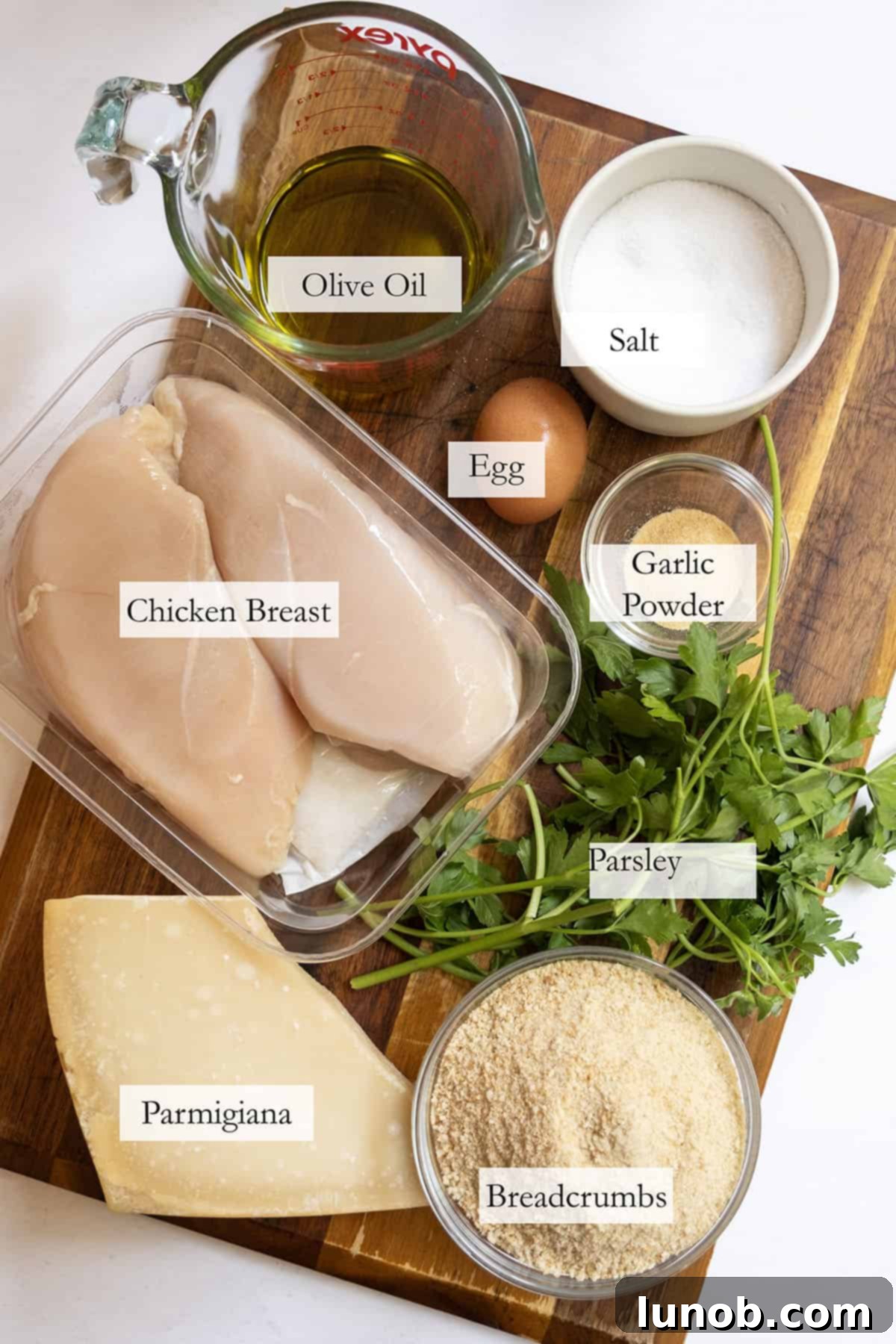 Fresh ingredients for Italian chicken cutlets laid out on a wooden board.