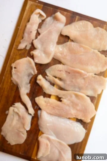 Thinly sliced chicken breast laid out on cutting board.
