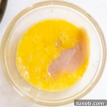 Chicken cutlet dipped in egg in bowl.