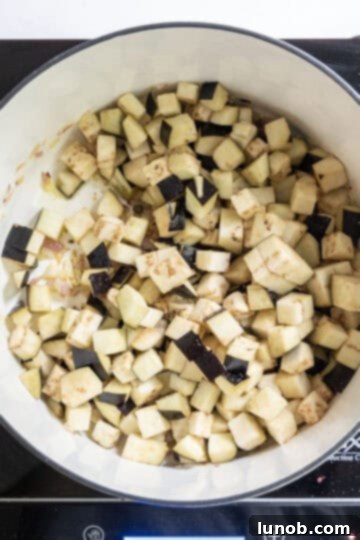 Chopped eggplant frying in a saucepan with onions and garlic