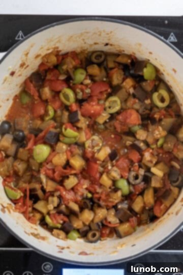 Eggplant caponata simmering in a pan, deepening its flavors