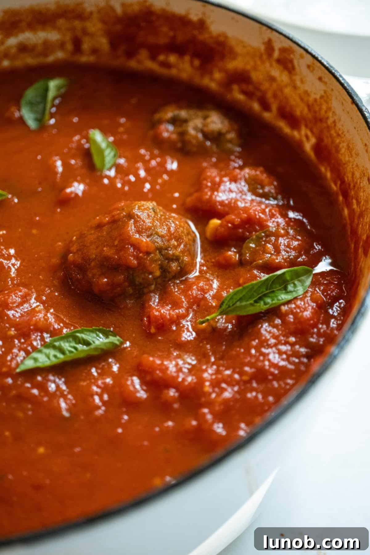 Nonna's Sunday Gravy 2 A rich, red Sunday sauce in a large pot, filled with tender meatballs and savory Italian sausages, ready to be served.