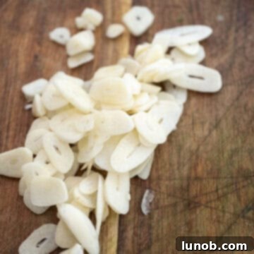 Nonna's Sunday Gravy 4 Fresh garlic cloves thinly sliced on a wooden cutting board, ready for cooking.