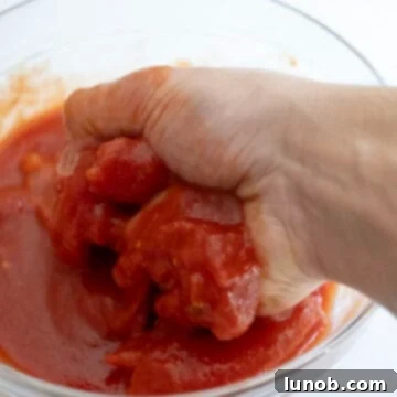 Nonna's Sunday Gravy 5 A hand gently crushing whole San Marzano tomatoes in a bowl, preparing them for the sauce.