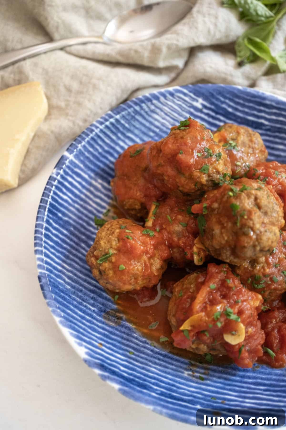A bowl of fried meatballs in tomato sauce, garnished with fresh basil and served alongside a block of Parmigiano cheese for grating.