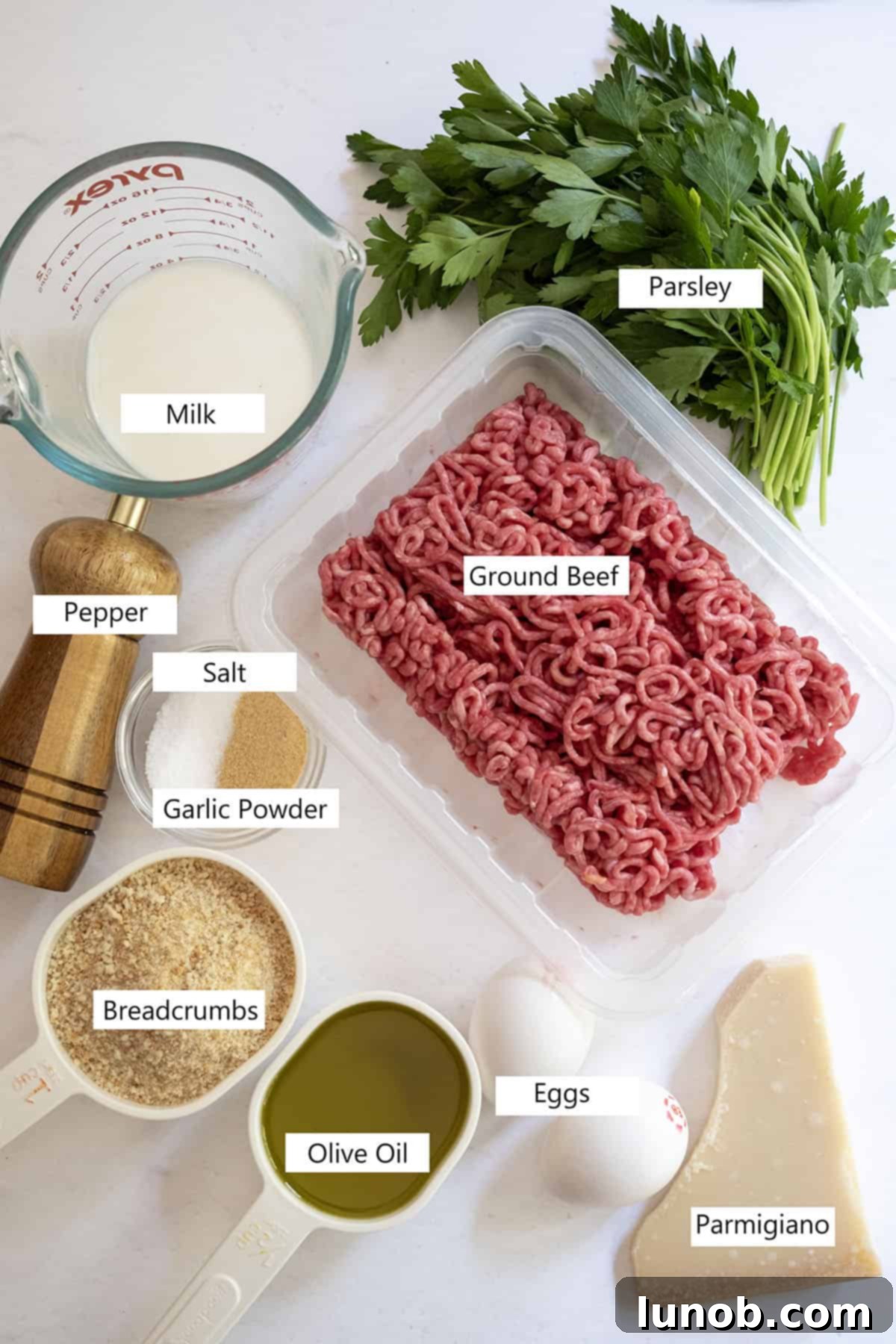 A selection of fresh ingredients laid out on a wooden board, including ground beef, parmesan cheese, parsley, eggs, and breadcrumbs, ready for making Italian Meatballs.