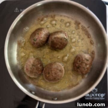 Browned meatballs frying in a saucepan, showcasing a crispy exterior after several minutes of cooking.