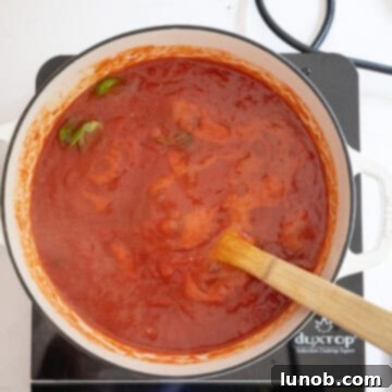 A rich red tomato sauce gently simmering in a pot on the stovetop, with fresh basil leaves adding aroma and flavor.