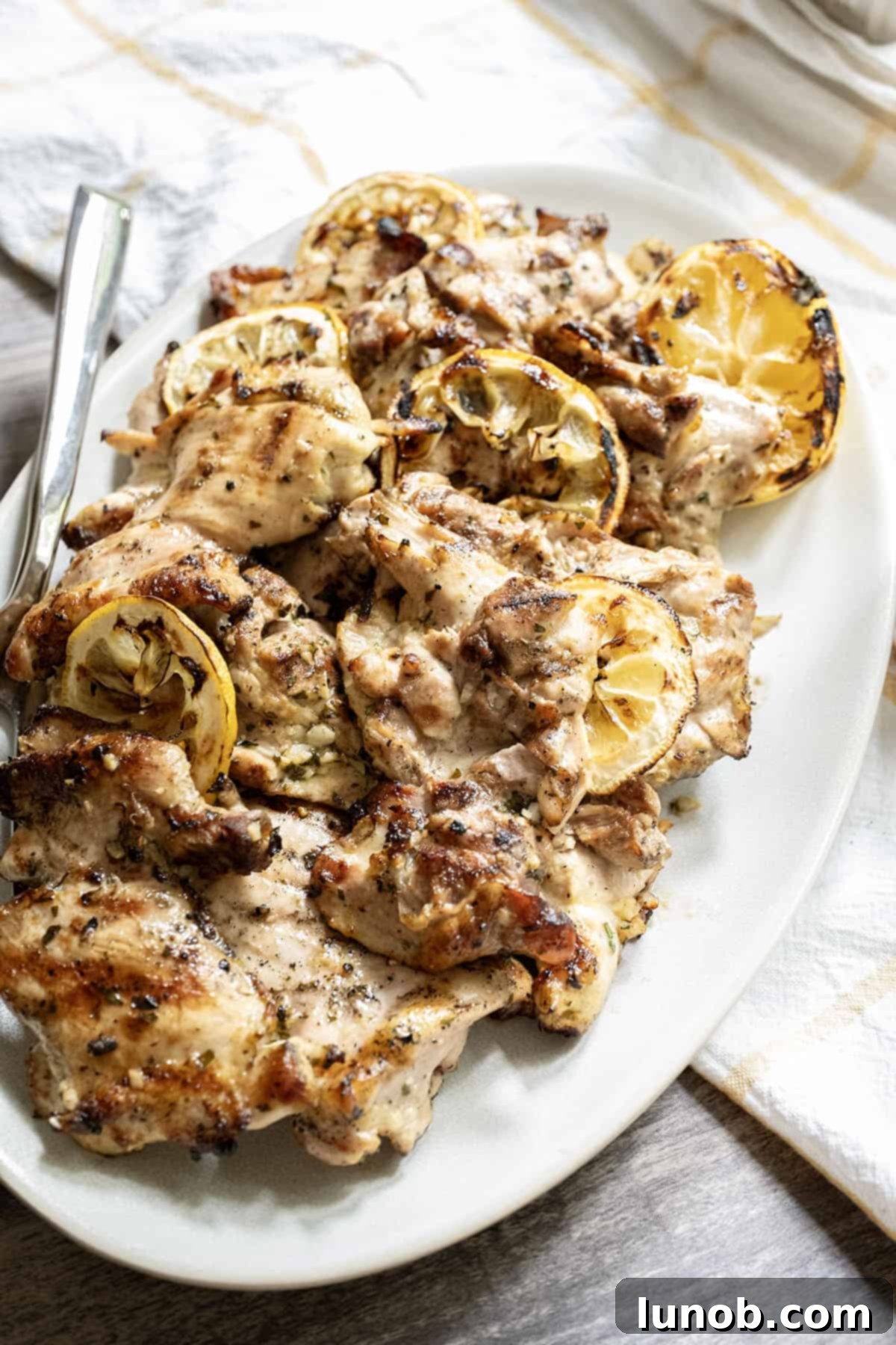 Zesty Grilled Lemon Pepper Chicken Thighs 2 Plate of perfectly grilled lemon pepper chicken thighs garnished with fresh lemon slices and herbs, ready to be served.