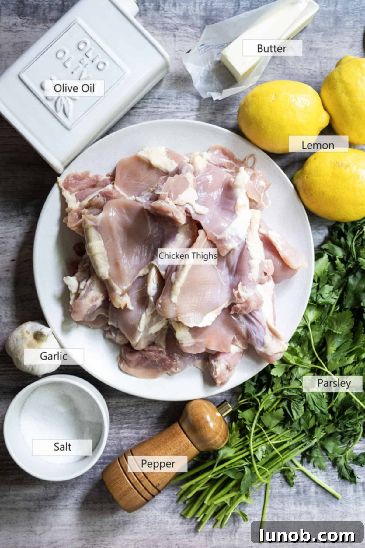 Zesty Grilled Lemon Pepper Chicken Thighs 3 Fresh ingredients laid out for grilled lemon pepper chicken, including whole lemons, minced garlic, fresh parsley, and a bottle of olive oil.