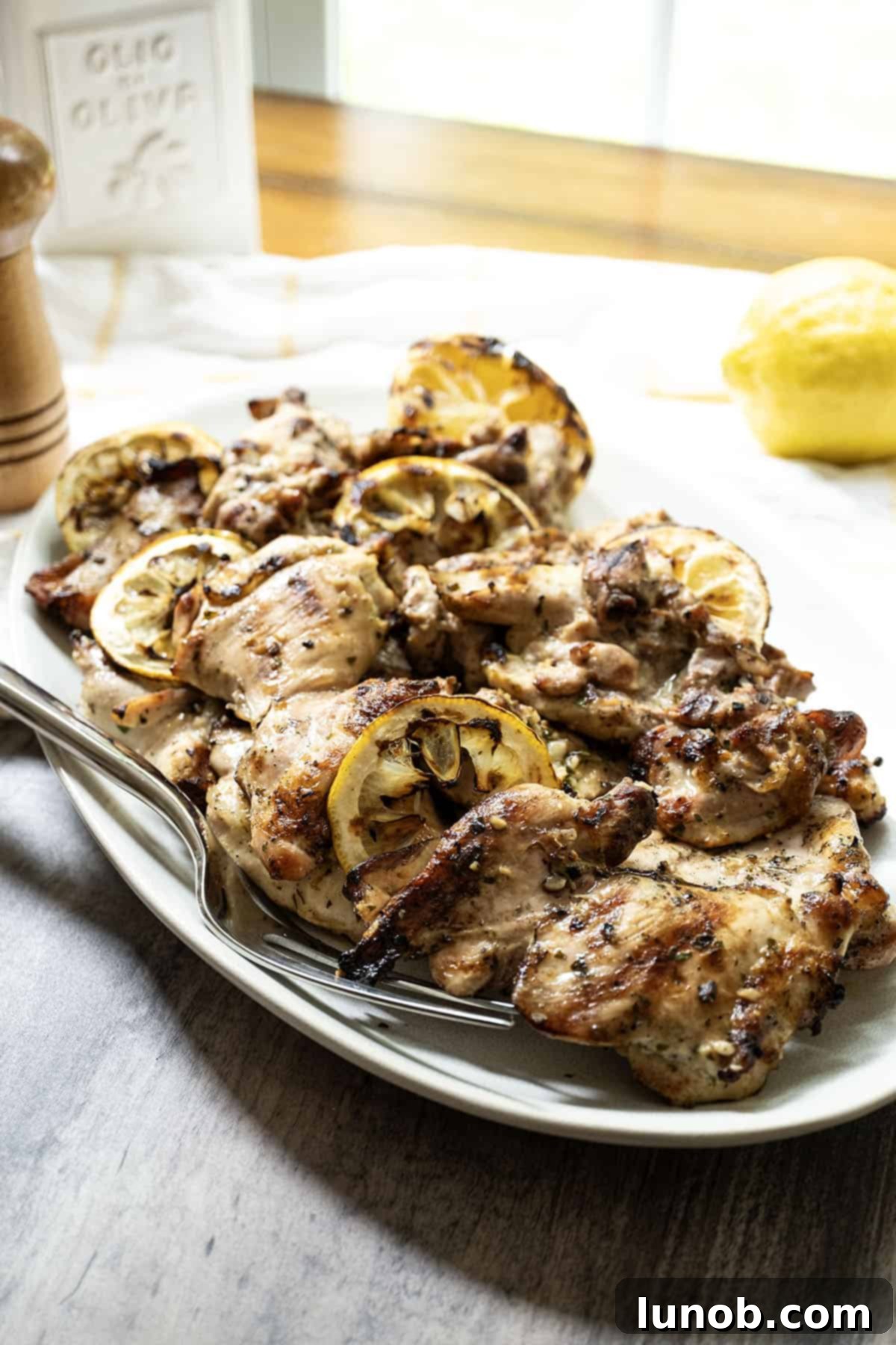 Zesty Grilled Lemon Pepper Chicken Thighs 8 Close-up of grilled lemon pepper chicken thighs garnished with fresh parsley and lemon wedges on a rustic white plate.