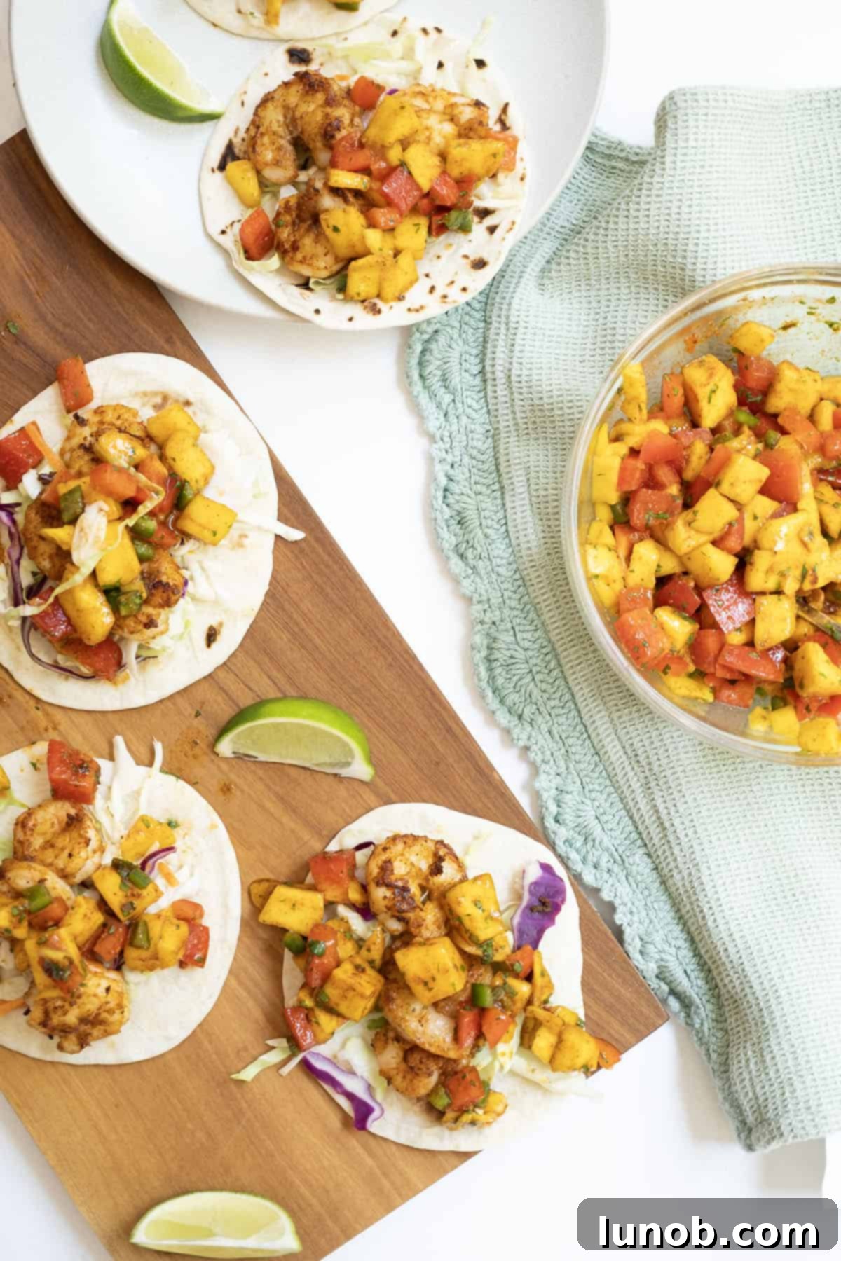 three shrimp tacos on white flour tortillas topped with mango salsa with a lime wedge in the middle. These tacos feature juicy, spiced shrimp and a colorful, fresh mango lime salsa, promising a burst of flavor in every bite.