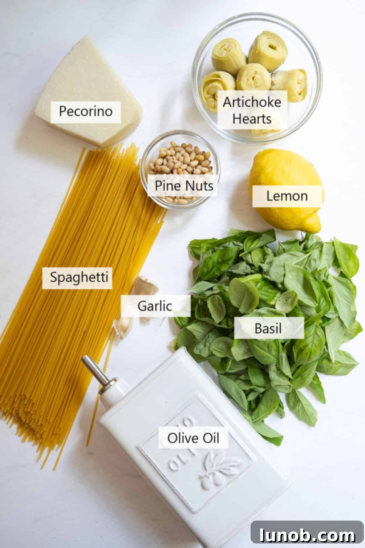 Mediterranean Artichoke Pesto Pasta 3 A flat lay photograph showcasing all the fresh ingredients for Artichoke Pesto Pasta, including basil, garlic, pine nuts, olive oil, parmesan, spaghetti, and artichoke hearts.