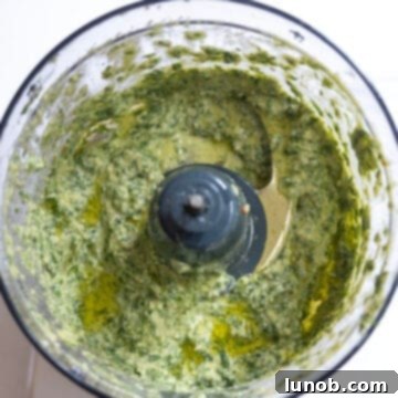 Mediterranean Artichoke Pesto Pasta 5 Olive oil being slowly drizzled into the pesto mixture in a food processor, creating a smooth emulsion.