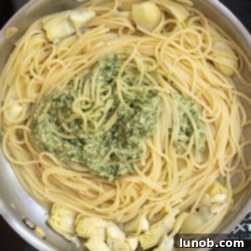 Mediterranean Artichoke Pesto Pasta 8 Freshly cooked spaghetti added to a large pan, with a dollop of artichoke pesto ready to be mixed.