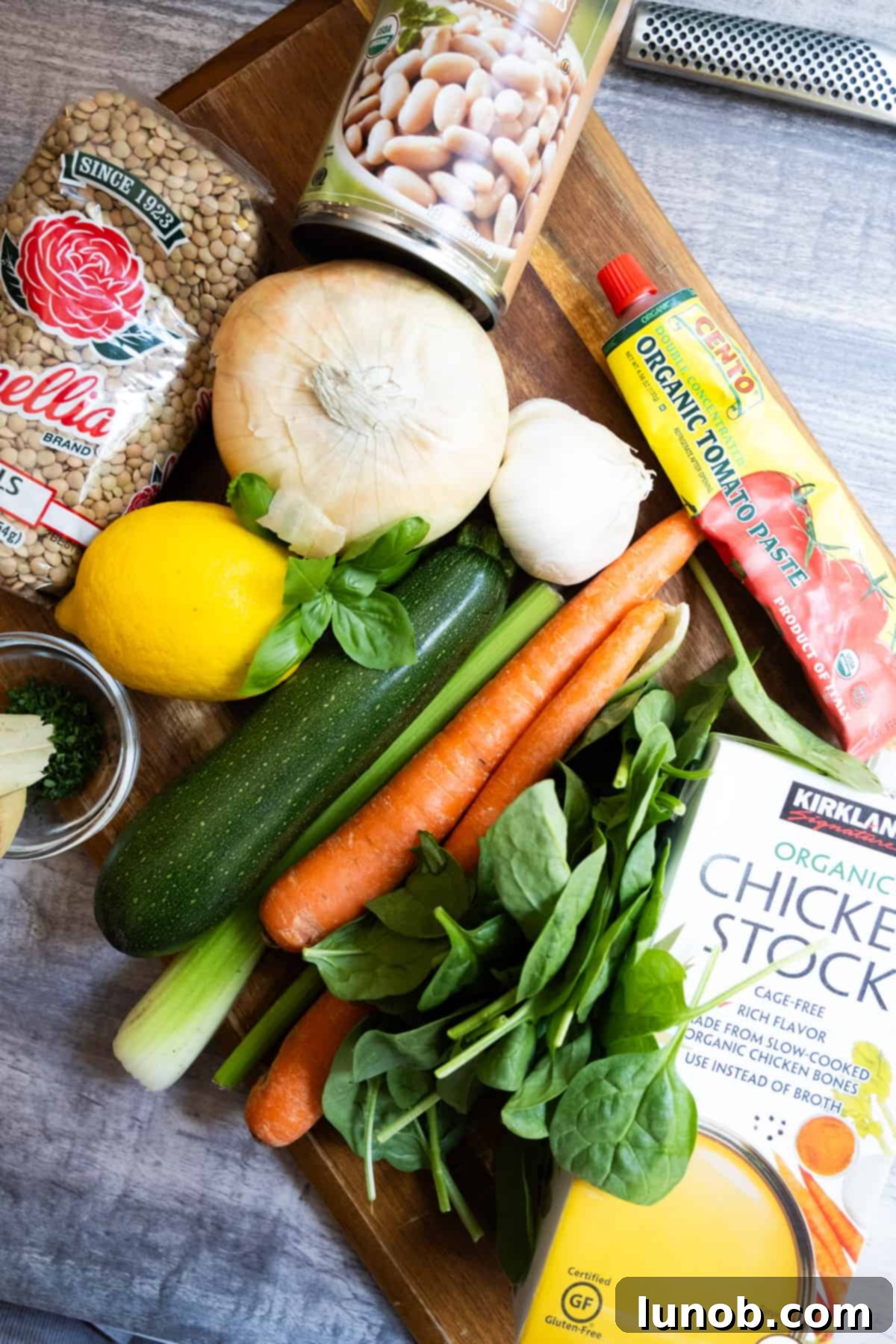 Hearty White Bean and Lentil Soup 3 A selection of fresh ingredients including carrots, celery, onion, garlic, lentils, and white beans, laid out on a wooden cutting board for a delicious homemade soup.