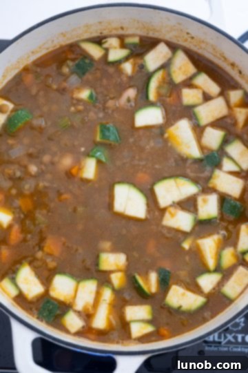 Hearty White Bean and Lentil Soup 9 Chopped zucchini and white beans being added to the simmering lentil soup for the final cooking stage.