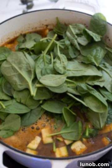 Hearty White Bean and Lentil Soup 10 Fresh spinach being stirred into the hot lentil soup, ready to wilt and add vibrant color.