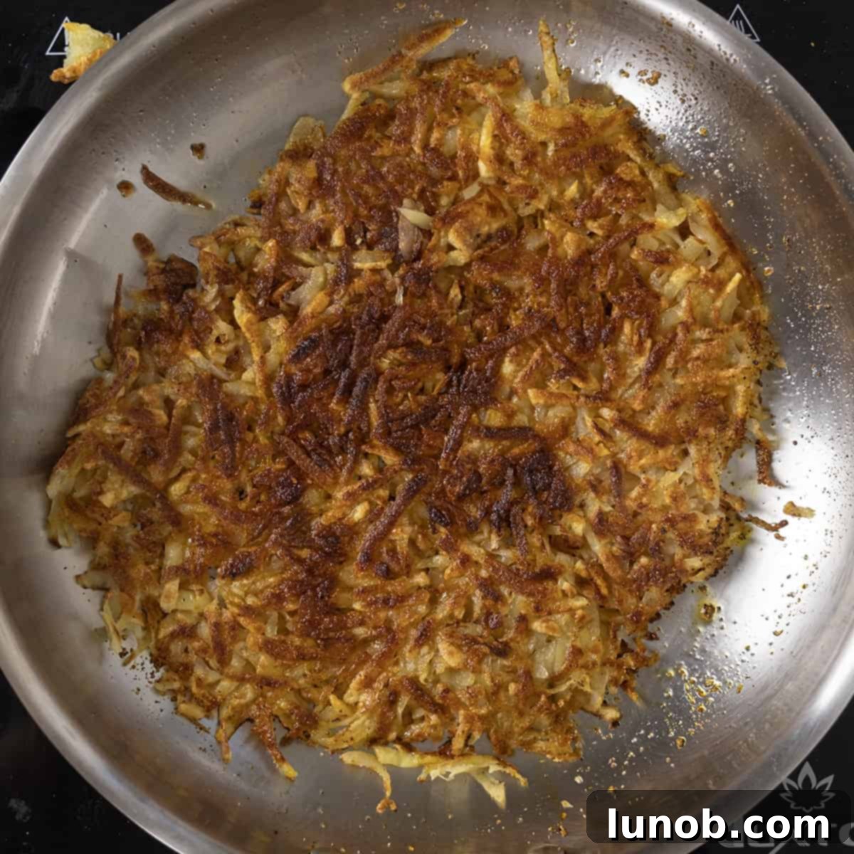 Hash browns flipped over in pan, revealing a crispy, golden-brown underside.