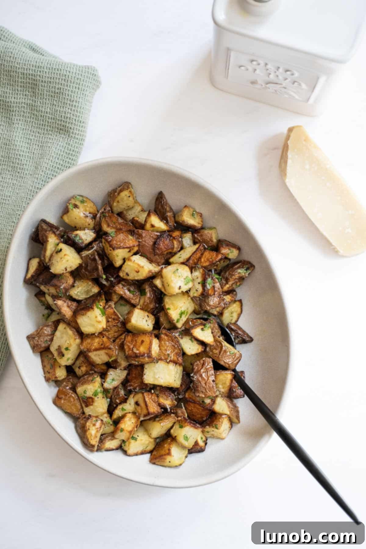 Ultimate Crispy Garlic Parmesan Potatoes 12 Crispy garlic parmesan potatoes in a bowl, with fresh parmesan and olive oil next to it.