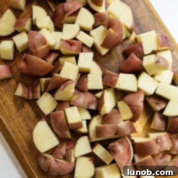 Ultimate Crispy Garlic Parmesan Potatoes 4 Chopped red potatoes on a cutting board, ready for seasoning.