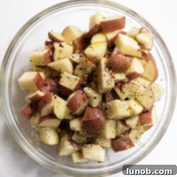 Ultimate Crispy Garlic Parmesan Potatoes 5 Seasoned potatoes in a bowl, coated with olive oil and spices.