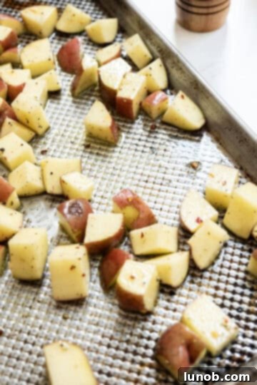 Ultimate Crispy Garlic Parmesan Potatoes 7 Seasoned potatoes being carefully added to a hot, oiled baking tray in a single layer.
