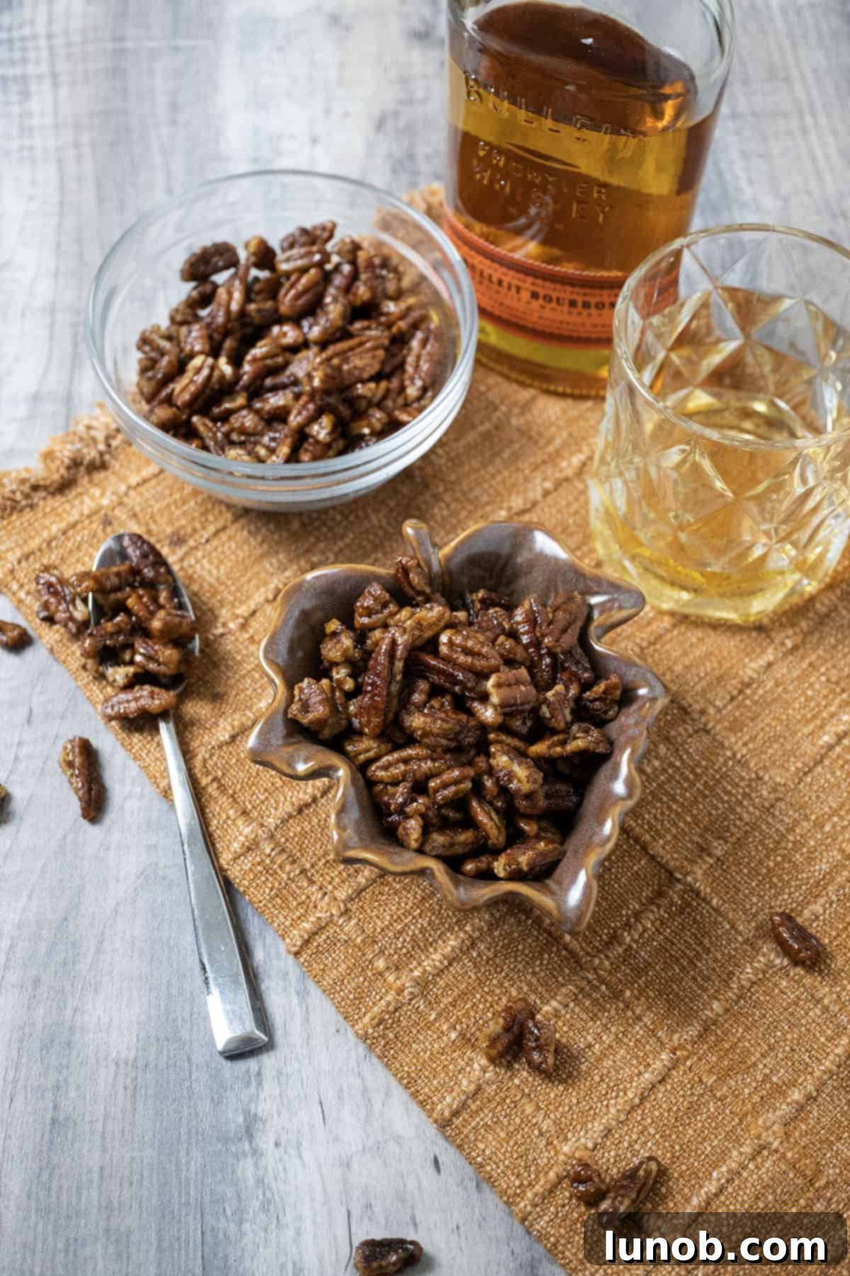 Candied pecans in 2 separate bowls next to a glass of bourbon.