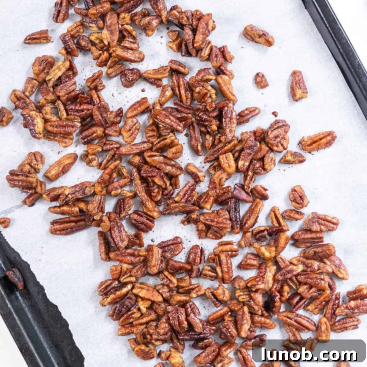 Pecans laid out on a parchment paper-lined baking tray.