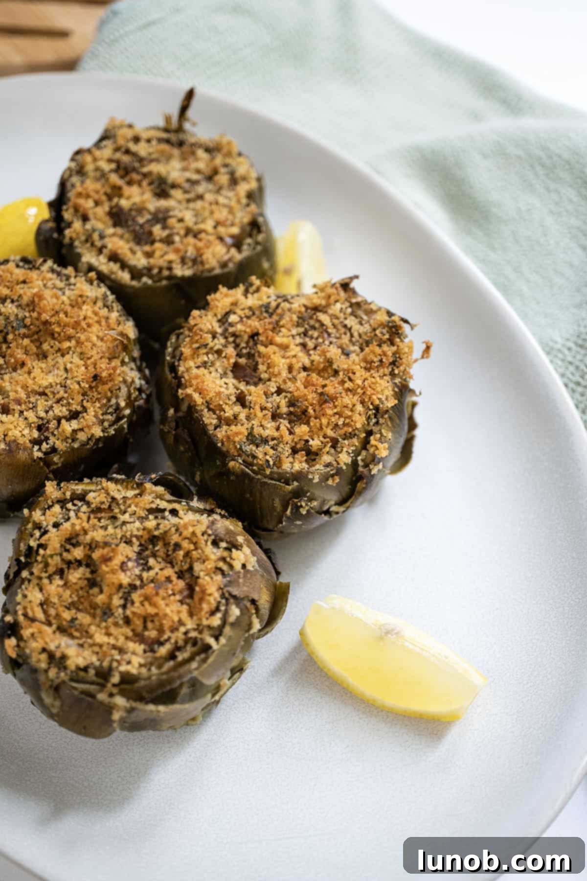 Two beautifully presented Italian stuffed artichokes with fresh lemon wedges.