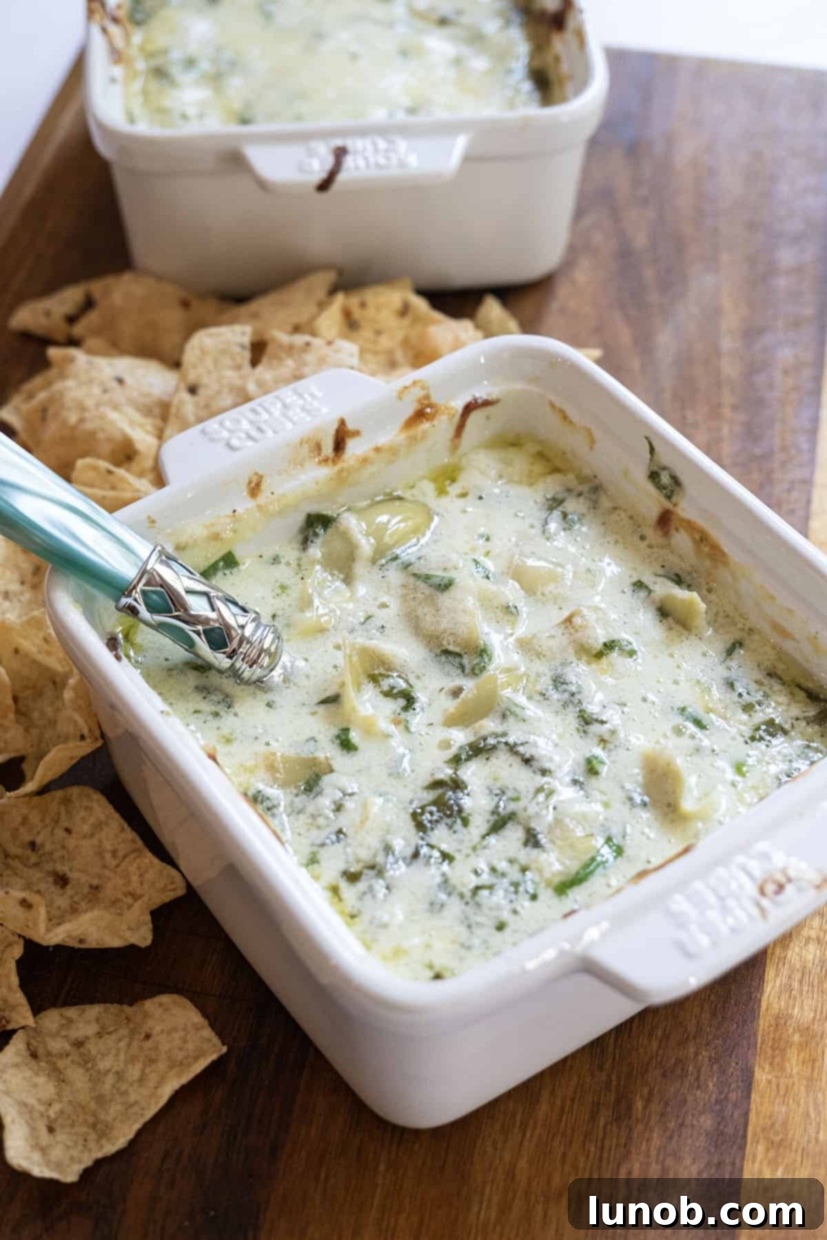 Creamy No-Mayo Spinach Artichoke Dip 2 Spinach and artichoke dip in a dish with some tortilla chips next to it.