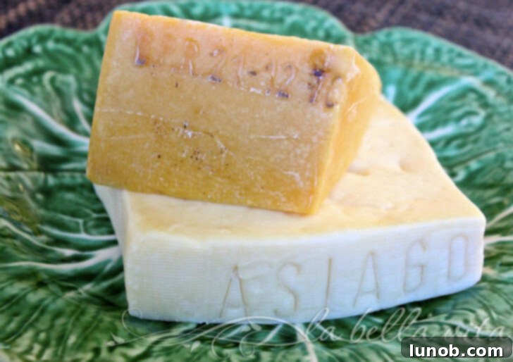 A block of Asiago cheese and grated Asiago, next to a knife on a wooden board.