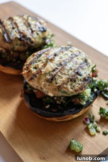 Grilled Greek chicken burger placed on a toasted bun with tabbouleh, ready for tzatziki.