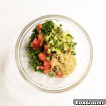 Freshly mixed tabbouleh ingredients in a bowl, showing vibrant parsley, bulgur, cucumber, and tomato.