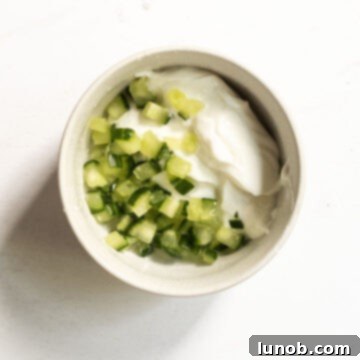 Simple tzatziki ingredients mixed together in a bowl, showcasing thick Greek yogurt and drained cucumber.