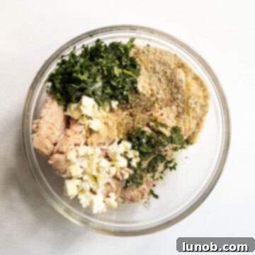 Ground chicken being mixed with feta, spinach, herbs, and other ingredients in a large bowl to form burger patties.