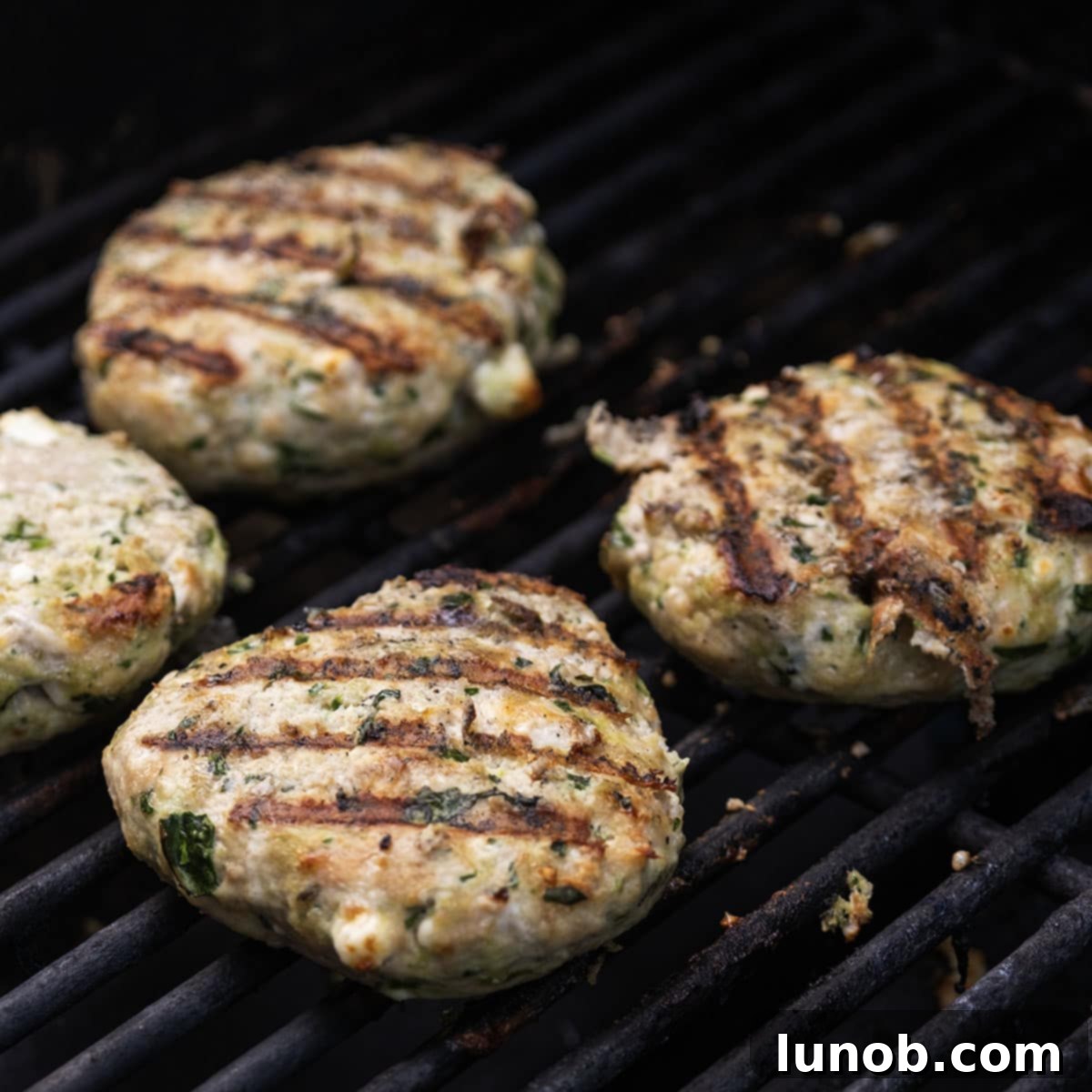Chicken patties cooking on a hot grill, showing distinct grill marks after being flipped.