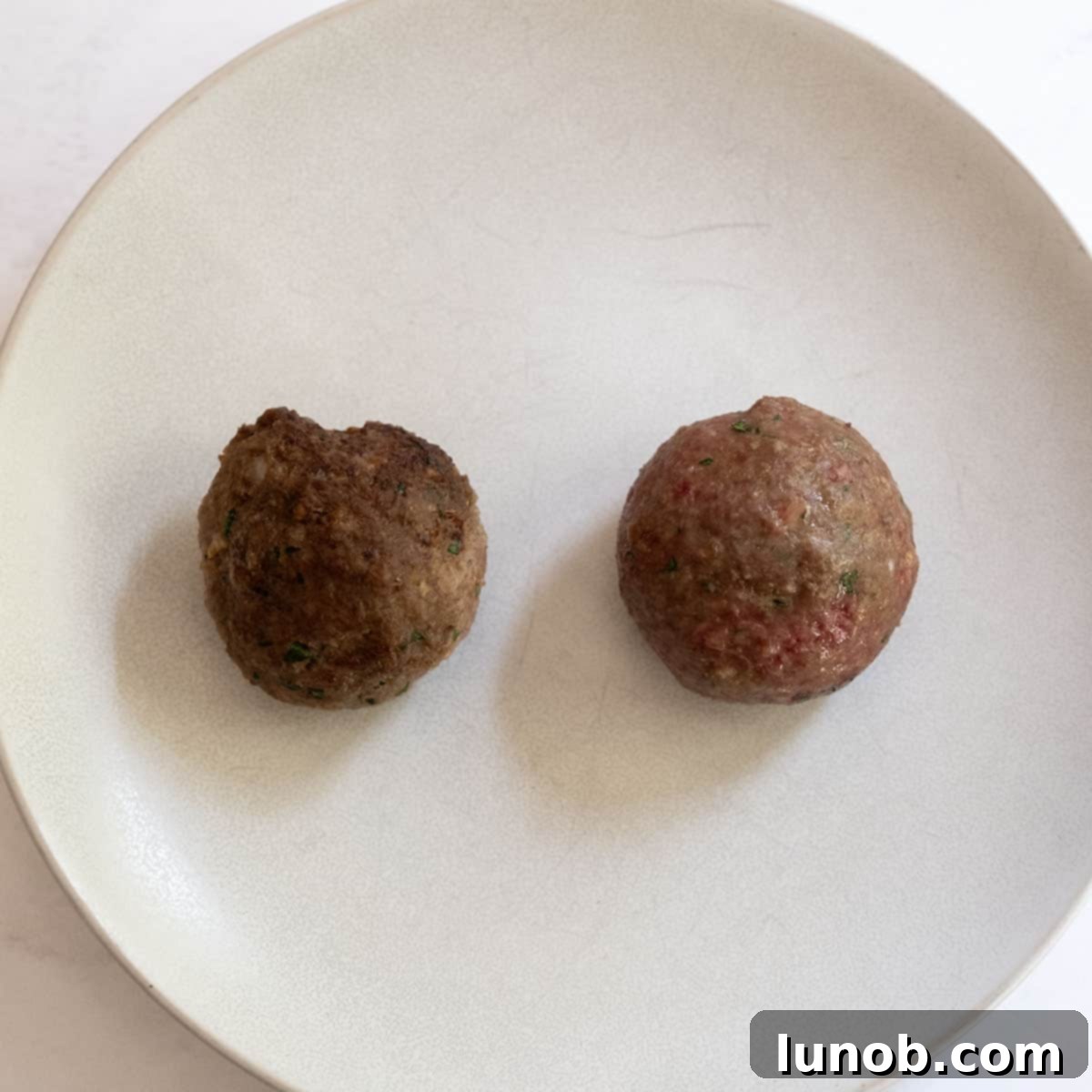 A comparison plate showing one baked and one fried meatball.
