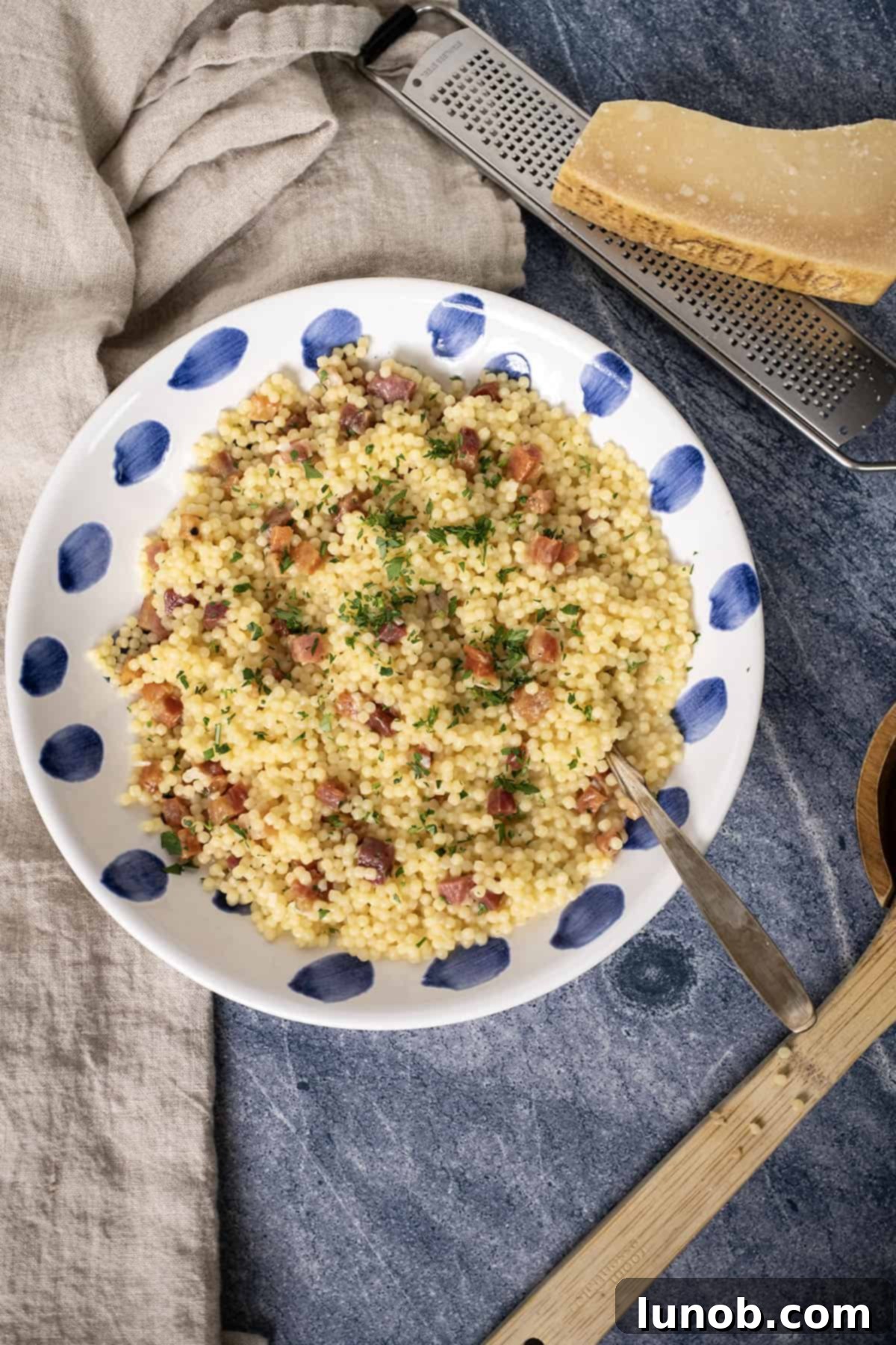 A beautifully presented bowl of creamy pastina carbonara, topped with crispy pancetta, a sprinkle of fresh parsley, and a wedge of lemon on the side.