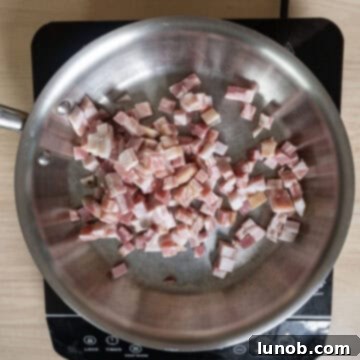 Diced pancetta placed in a cold stainless steel pan, ready to be heated.