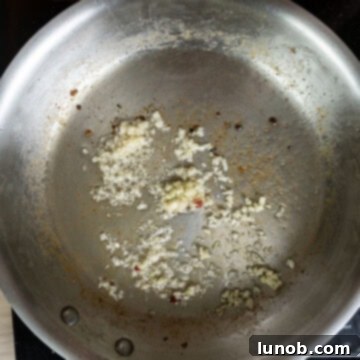Minced garlic cloves gently sizzling in the rendered pancetta fat in a pan, releasing their aromatic fragrance.