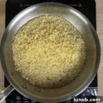 Cooked pastina and a ladleful of pasta water being added to a pan with fragrant sautéed garlic, starting to form the creamy sauce base.
