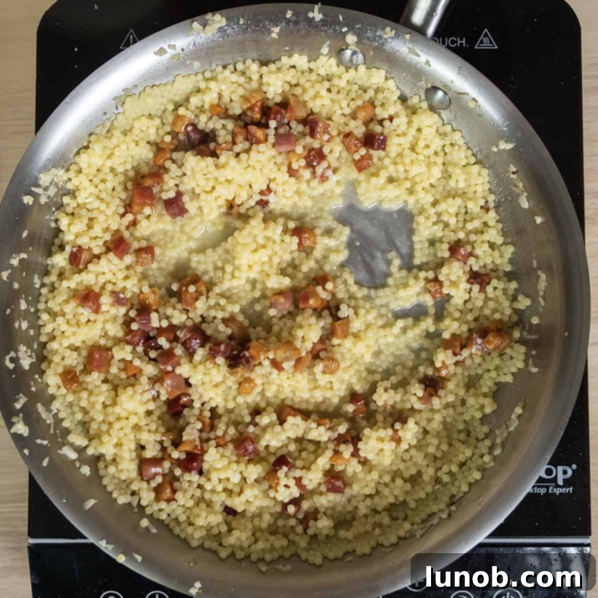 Freshly grated Parmigiana cheese and crispy pancetta being added to the pastina in the pan, stirred together to create a rich and creamy sauce.