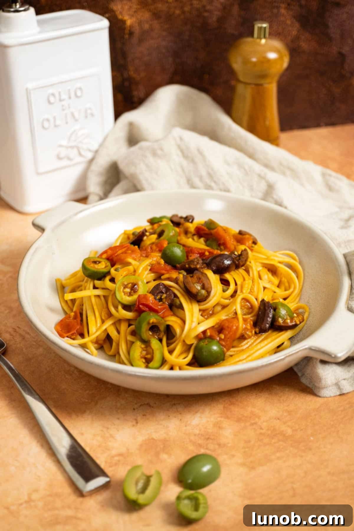 Linguine puttanesca topped with olives and capers in a bowl, ready to be served.