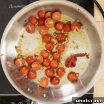 Halved cherry tomatoes bursting and combining with garlic and tomato paste in a pan.