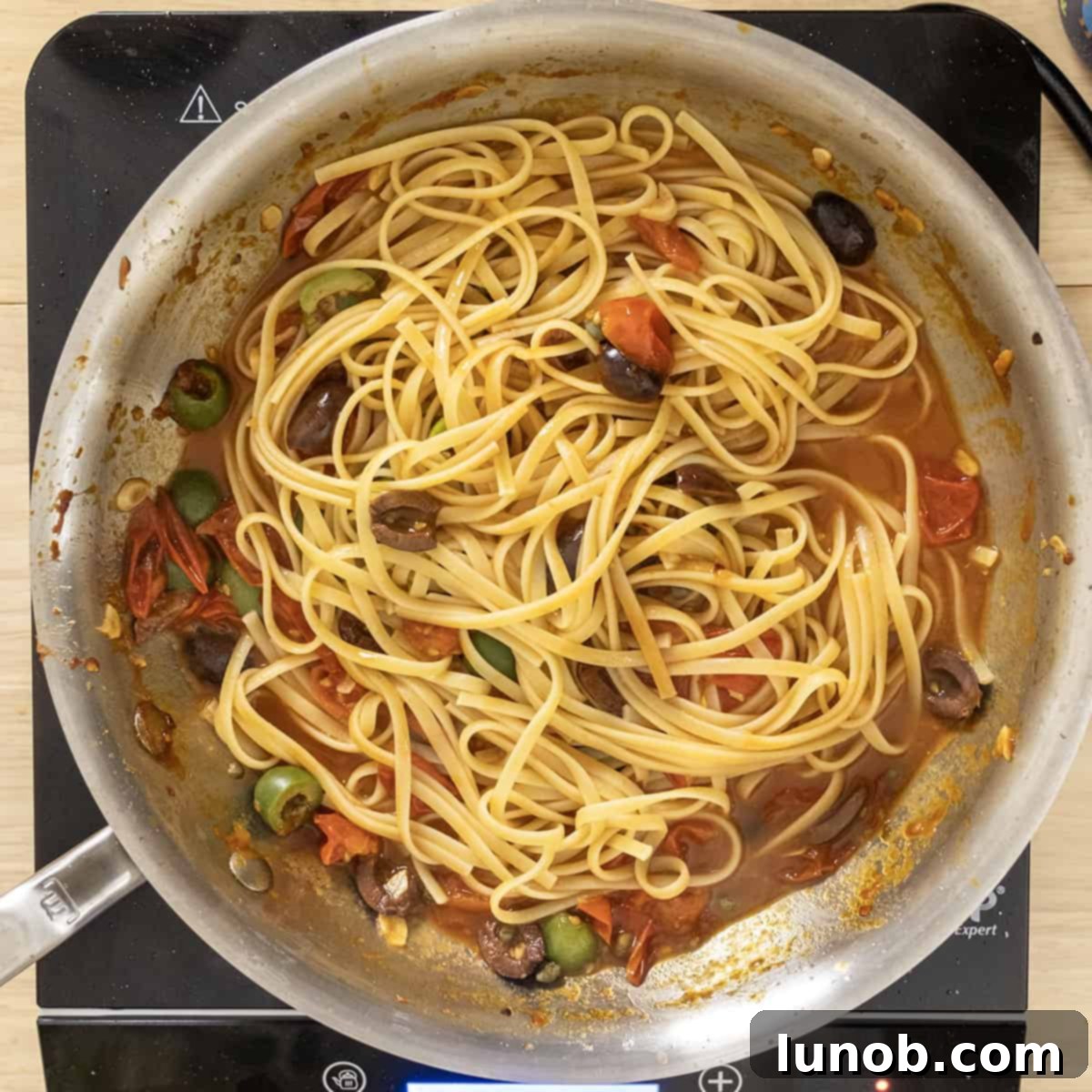 Al dente pasta combined with rich puttanesca sauce in a saucepan.