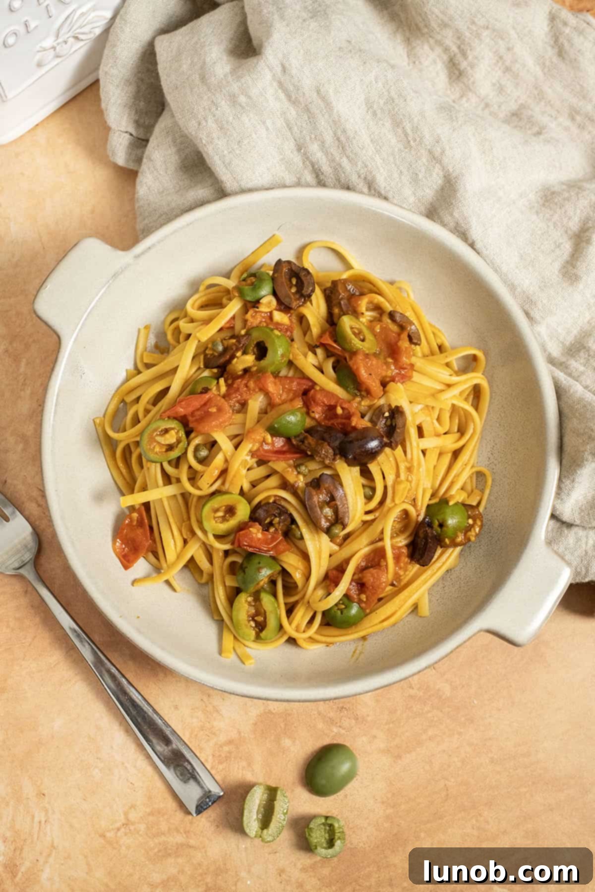A beautifully plated bowl of Linguine Alla Puttanesca garnished with fresh parsley and extra olives.