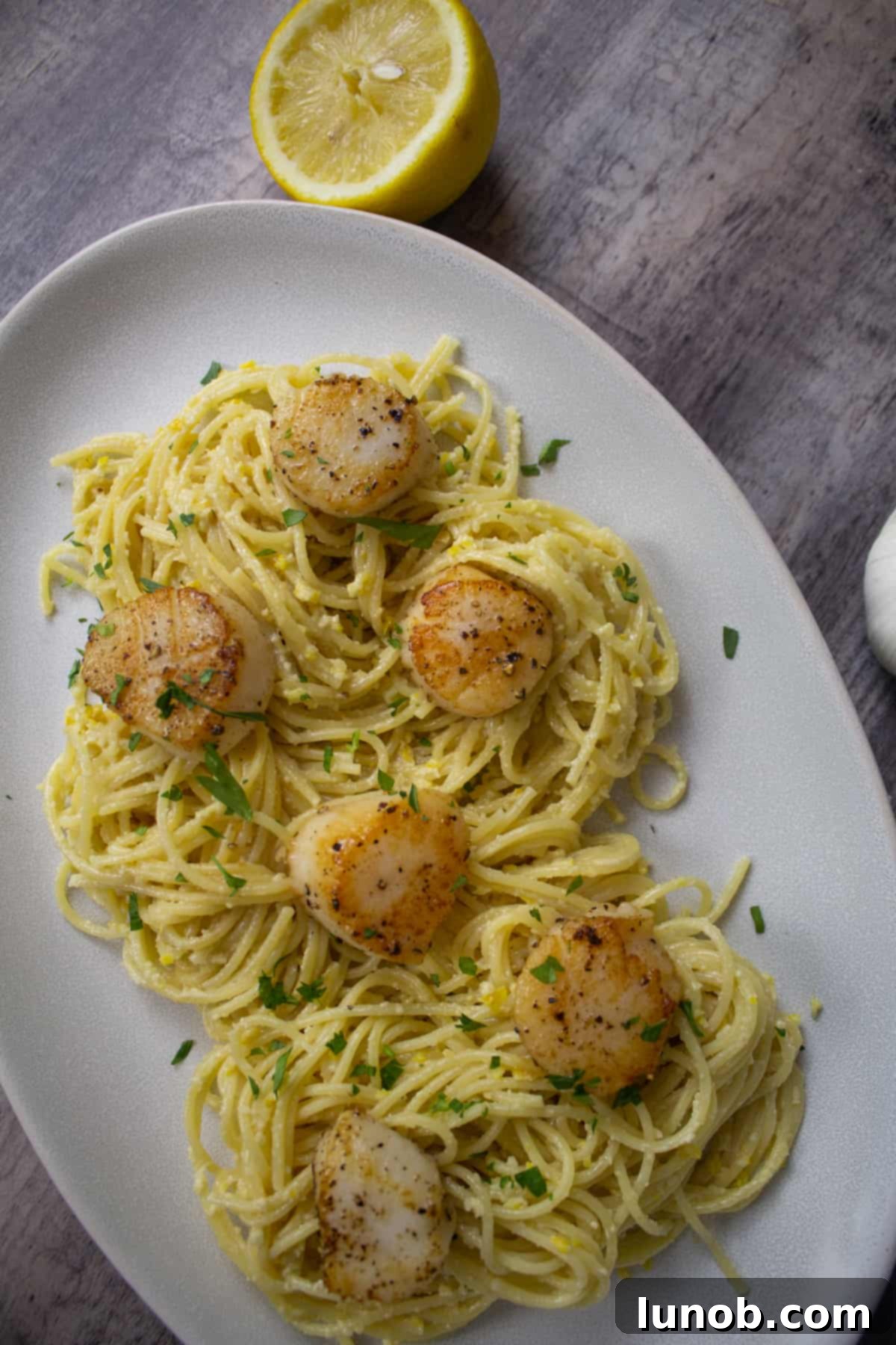 lemon pesto spaghetti with scallops and a lemon half.
